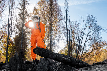 Astronaut in an orange suit on the ruins of a burnt-out building. The charred remains of a wooden house at the disaster site.の写真素材