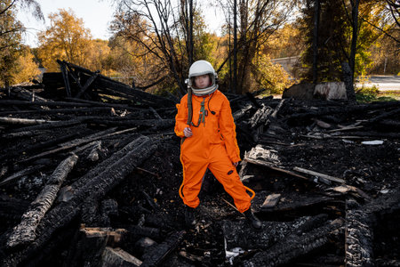 Astronaut in an orange suit on the ruins of a burnt-out building. The charred remains of a wooden house at the disaster site.の写真素材
