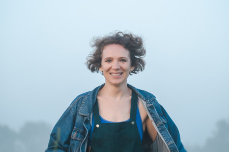 Curly haired 30 year old woman in a dress walks in the morning misty field.の写真素材