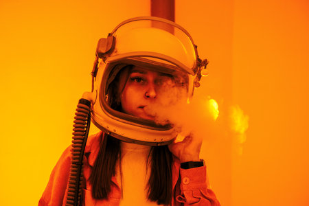 Woman in an astronaut helmet, with smoke emerging, stands against a bright orange background, evoking space exploration and mystery.の写真素材