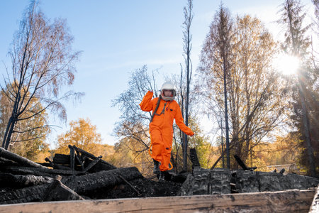 Astronaut in an orange suit on the ruins of a burnt-out building. The charred remains of a wooden house at the disaster site.の写真素材