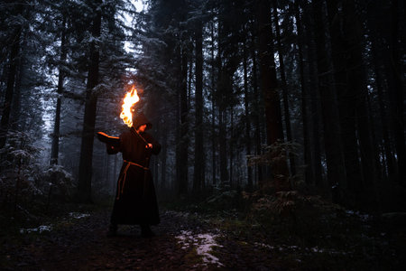 Sorcerer in cloak black and torch is conjuring in a winter forest against a background of thick smoke.の写真素材