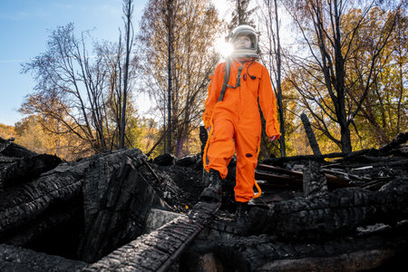 Astronaut in an orange suit on the ruins of a burnt-out building. The charred remains of a wooden house at the disaster site.の写真素材