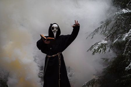A person in a mask is performing a ritual in a winter forest against a background of thick smoke.の写真素材