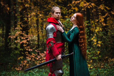 Medieval knight in armor and princess in green dress embrace in a forest setting.の写真素材