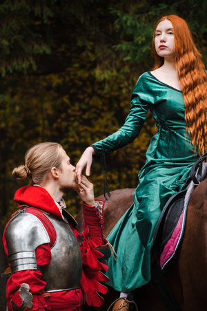 Knight in armor holding a princess hand on horseback in a magical autumn forest.の写真素材