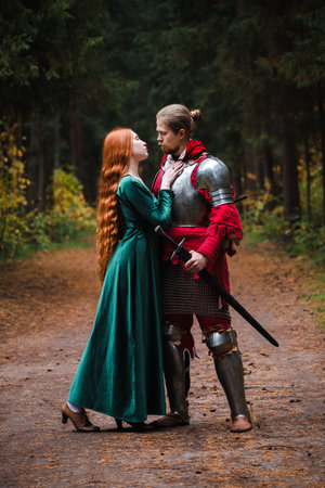 Medieval knight in armor and princess in green dress embrace in a forest setting.の写真素材