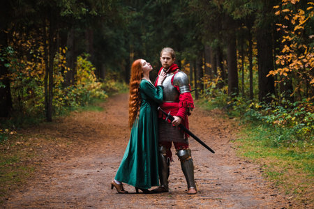 Medieval knight in armor and princess in green dress embrace in a forest setting.の写真素材