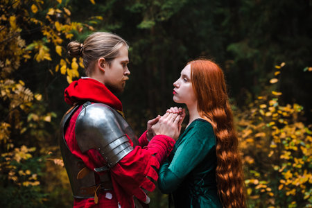 Medieval knight in armor and princess in green dress holding hands in a forest setting.の写真素材