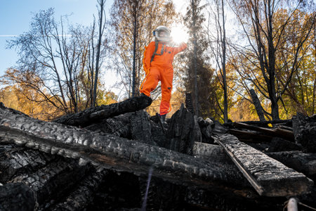 Astronaut in an orange suit on the ruins of a burnt-out building. The charred remains of a wooden house at the disaster site.の写真素材