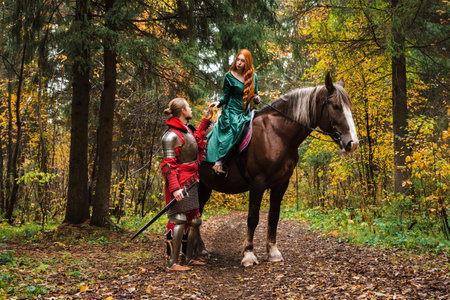 Knight in armor holding a princess hand on horseback in a magical autumn forest.の写真素材