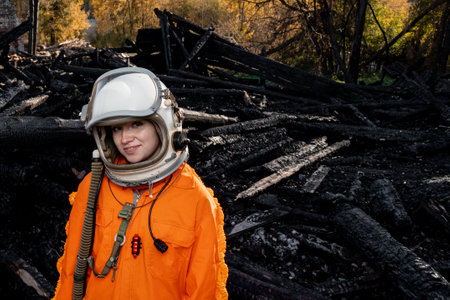 Astronaut in an orange suit on the ruins of a burnt-out building. The charred remains of a wooden house at the disaster site.の写真素材