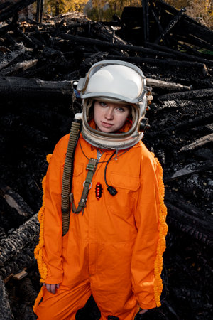 Astronaut in an orange suit on the ruins of a burnt-out building. The charred remains of a wooden house at the disaster site.の写真素材