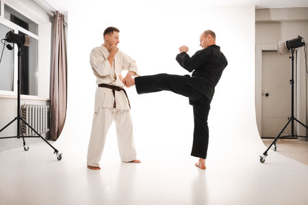 Two martial artists practicing karate, one delivering a kick, wearing black and white kimono.の写真素材