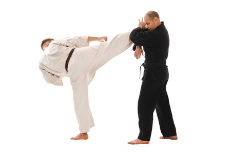 Two martial artists practicing karate, one delivering a kick, wearing black and white kimono.の写真素材