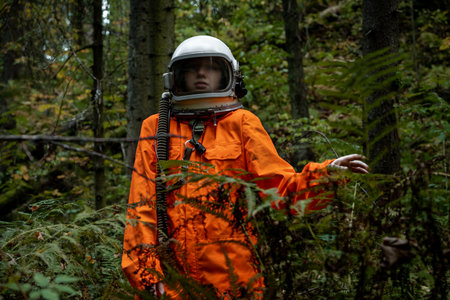 Astronaut in orange suit exploring dense forest wearing helmet, mysterious and surreal atmosphere.の写真素材
