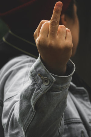 Close-up of a woman showing a middle finger gesture while wearing a denim jacket.の写真素材