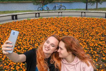 Two smiling women taking a selfie in a vibrant field of orange flowers outdoors.の写真素材