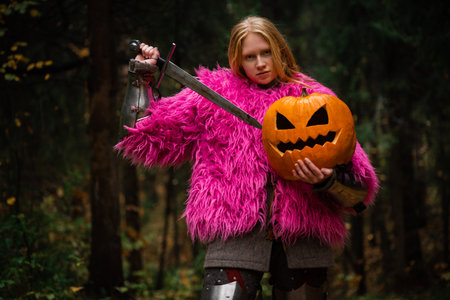 A woman knight in medieval armor and a pink fur coat jacket stands on a forest path, holding a...