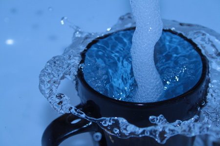 Clear blue water splashing out of the ceramic cupの写真素材