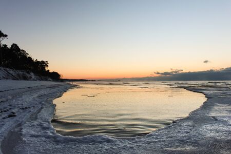 Pink tone of sunset on sky, snowy beach and old wooden pierの写真素材