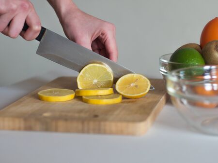 Woman cutting the lemon into thin pieces on wooden board for making a drink