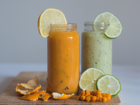 Healthy orange nad green smoothie with orange and sea-buckthorn on the wooden boardの写真素材
