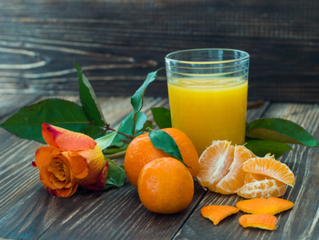 Glass of fresh orange juice and rose on wooden table.の写真素材