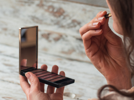 young beautiful woman applying her make-up, looking in a mirror. Close upの写真素材