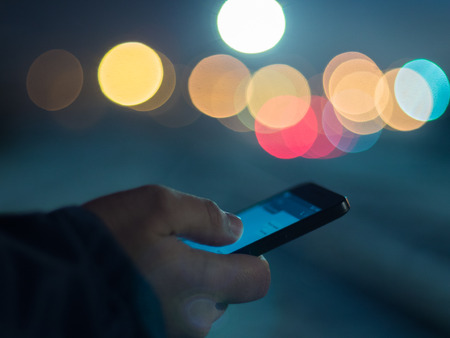 Man using smartphone at night, bokeh light in blurred background.の写真素材