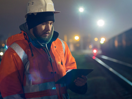 Young and handsome worker using tablet during hignt. In helmet and reflective jacketの写真素材