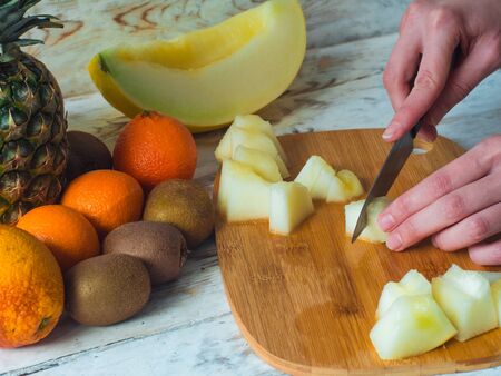 Close up woman hands cutting fresh melon with knife on wooden chopping board. Female cutting fruits.の写真素材