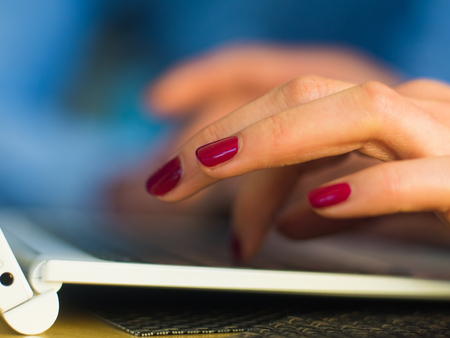 Woman's hands typing on laptop keyboard in interior, side view of businessman using computer in cafe.の写真素材