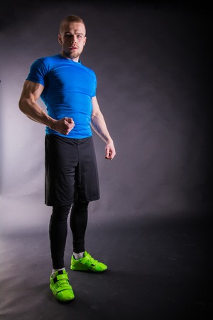 Full length portrait of a muscular man in sports wear standing on a dark background and looking at camera.の写真素材