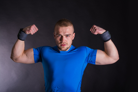Front view portrait of a young fitness man standing with arms up over dark studio backgroundの写真素材