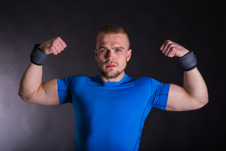 Front view portrait of a angry man standing showing his muscles over dark studio backgroundの写真素材