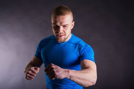 Muscular young man in sports outfit arms punching, smiling on dark background.の写真素材