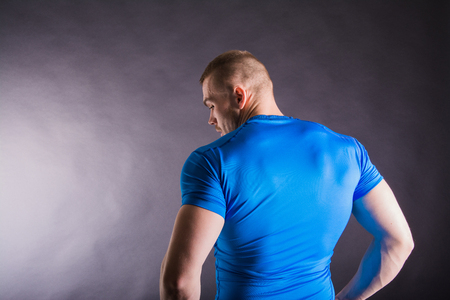 Back view of a muscular young man standing in studio on dark background.の写真素材
