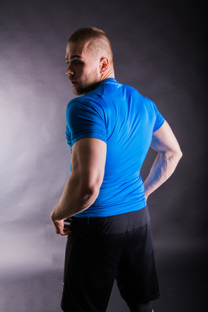 Back view of a muscular young man standing in studio on dark backgroundの写真素材