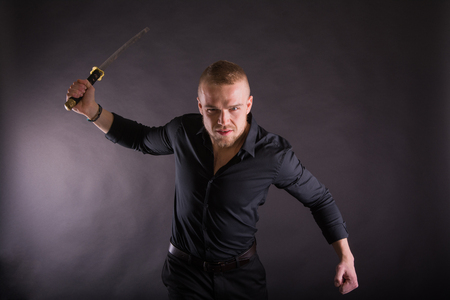 Aggressive young man holding katana sword Looking at the Camera Against Wall Background.の写真素材