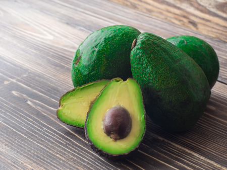 Ripe avocado with slices on dark old wooden table, side view.