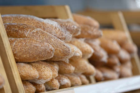 A lot of toasted baguettes with sesame and crispy crust in polyethylene packaging are lying on...