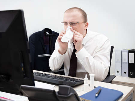 Man working in office on a computer in a white business shirt and red tie have got running nose and blows his nose to a napkin, close upの写真素材