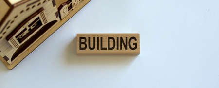 Wooden block form the word 'building' near miniature house. Beautiful white background, copy space.の写真素材