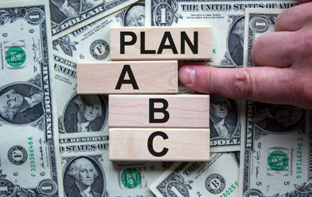 Wooden blocks form the words 'plan, a, b, c,' on background from dollar bill. Male hand. Beautiful...