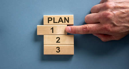 Wooden blocks form the words 'plan, 1, 2, 3,' on blue background. Male hand. Beautiful background.