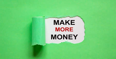 The text 'make more money' appearing behind torn green paper.の写真素材