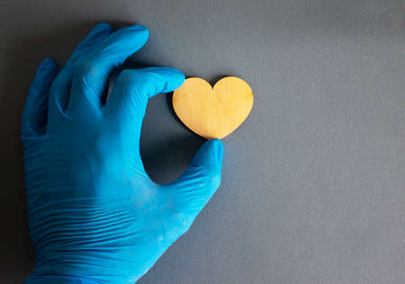 Wooden heart, hand in blue glove on blue background.の写真素材
