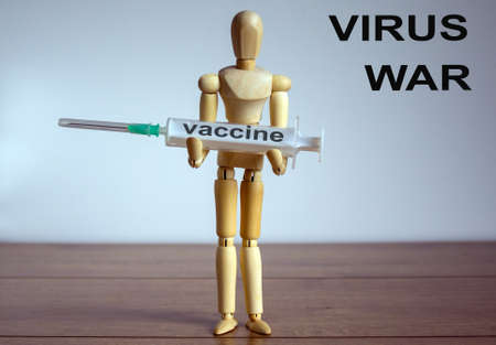 Pandemic Coronavirus concept  Wooden model of a man holding a holding a syringe labeled vaccine. "Virus war " inscription.の写真素材