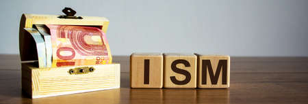 Concept word ISM on cubes on a beautiful wooden table, small chest with euro bills.の写真素材